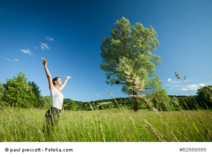 Young beautifull woman relaxing with arms raised in nature with tree in background and grass in foreground.